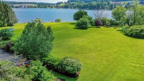 A well-maintained lawn with a gazebo, a lake view, and a parking area with cars.