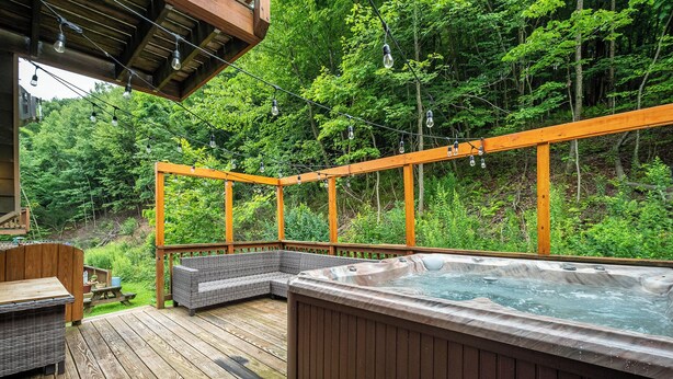 Eine Holzterrasse mit Whirlpool, Korbmöbeln und einer Pergola mit Lichterketten.