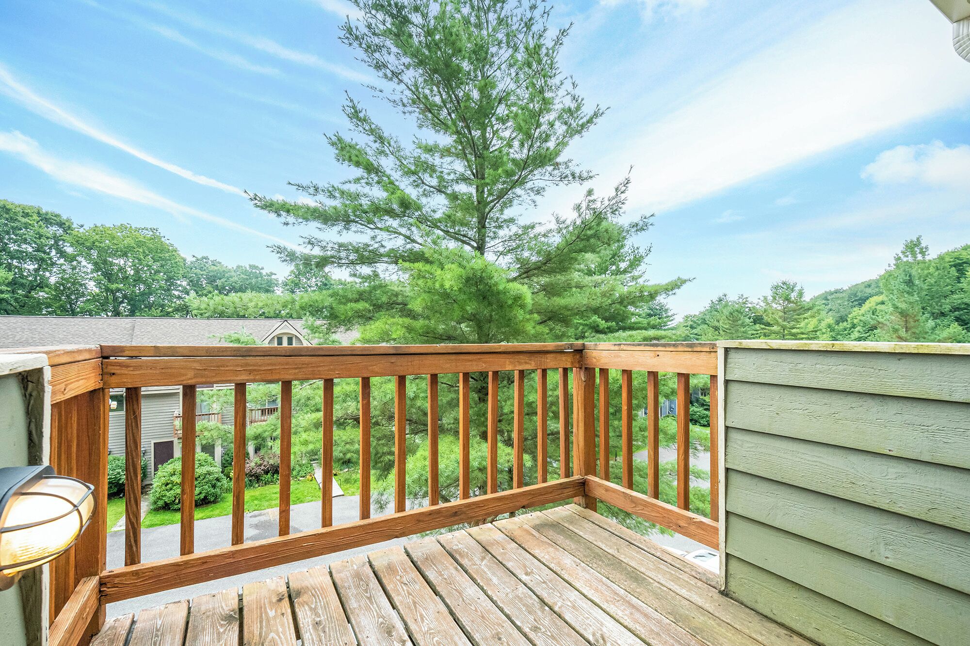 A wooden deck with a railing, a light fixture, and a view of a green landscape with trees.