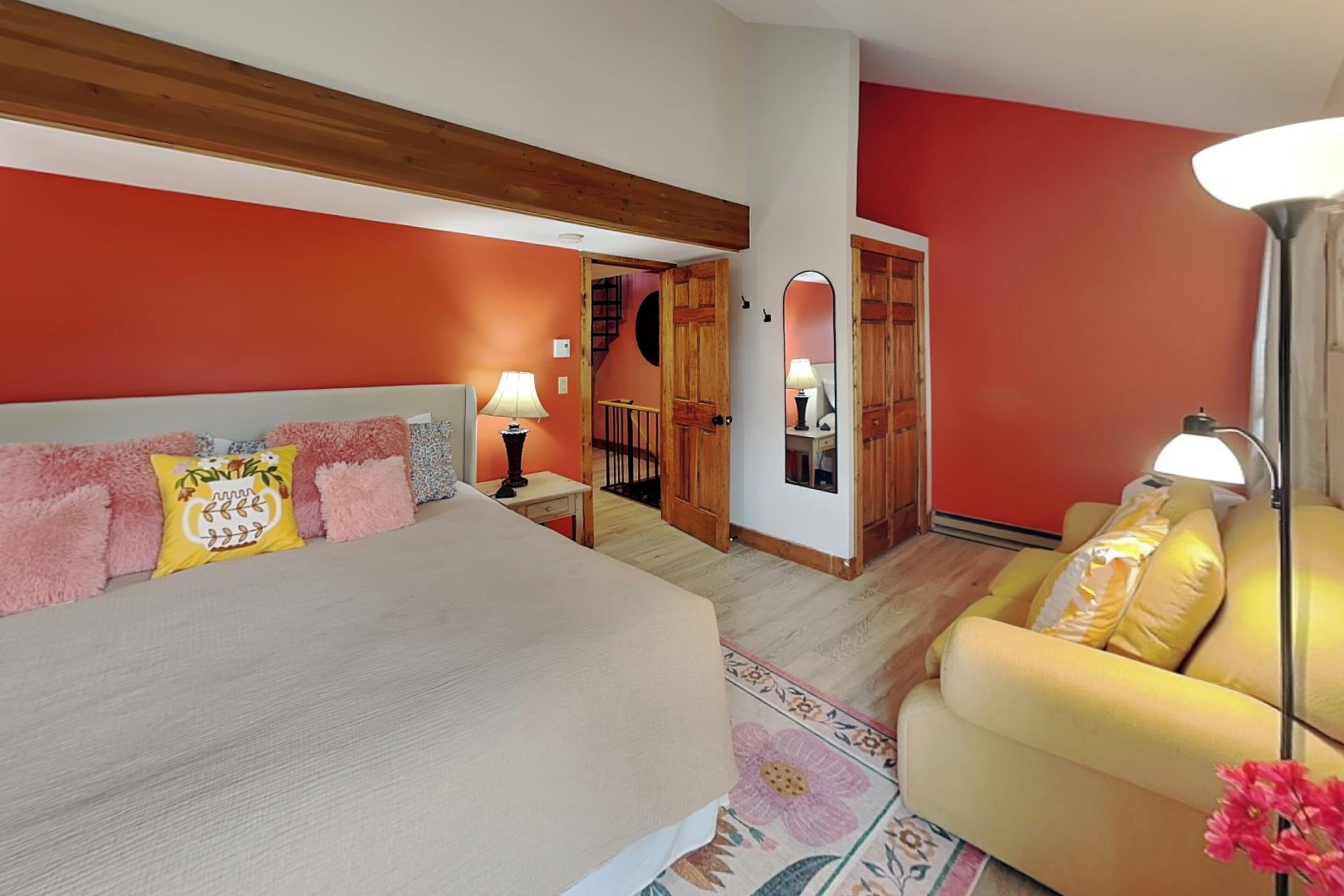 A bedroom with a bed, a nightstand, a lamp, a sofa, and a mirror.