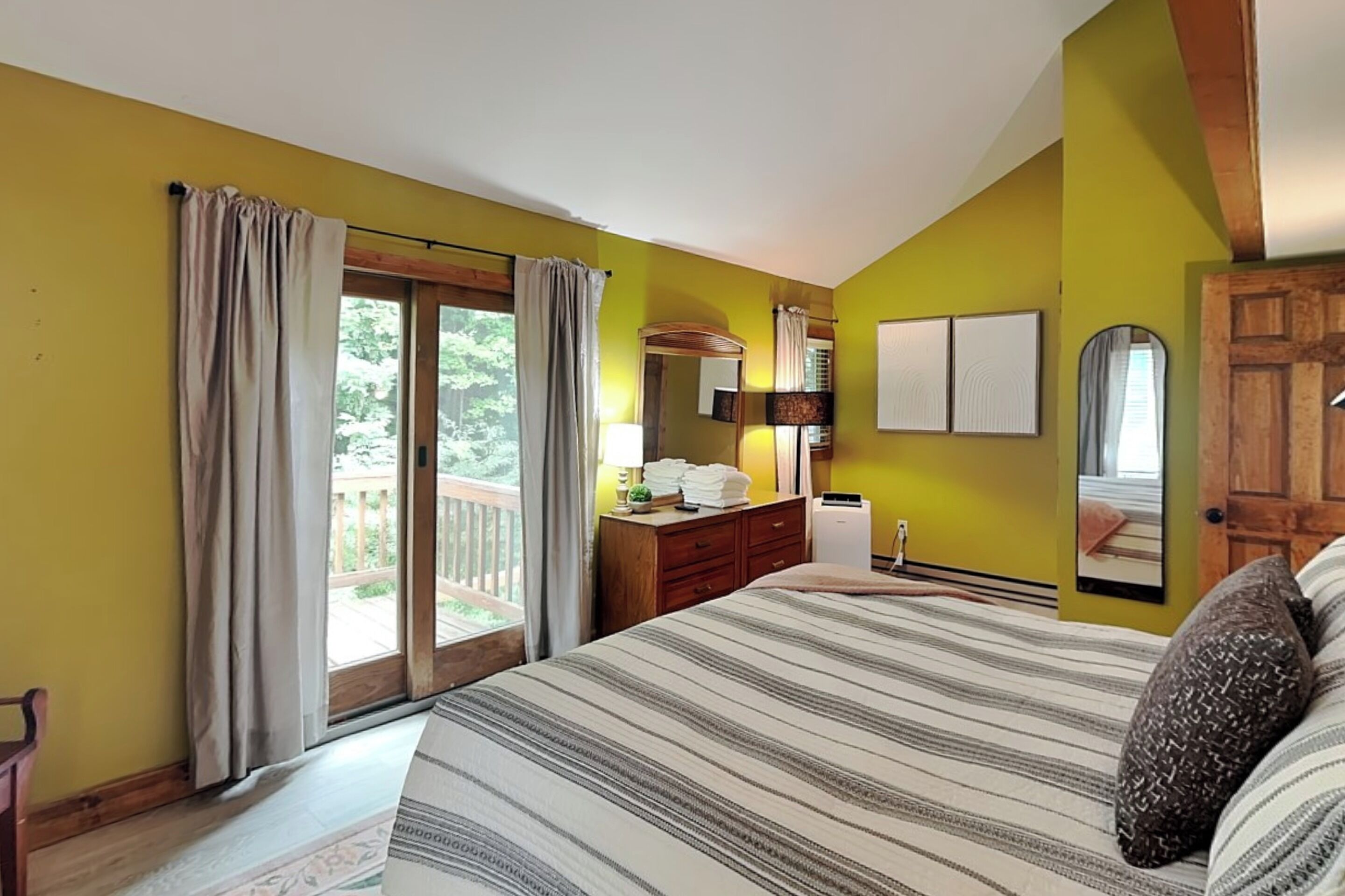 Un dormitorio con una cama grande, un aparador, un espejo y una ventana con cortinas.