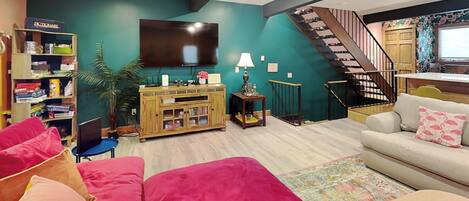 A living room with a sofa, a television, a bookshelf, and a staircase.