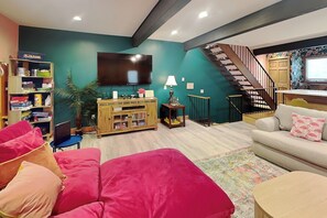 Uma sala de estar com um sofá, televisão, estante e escada.