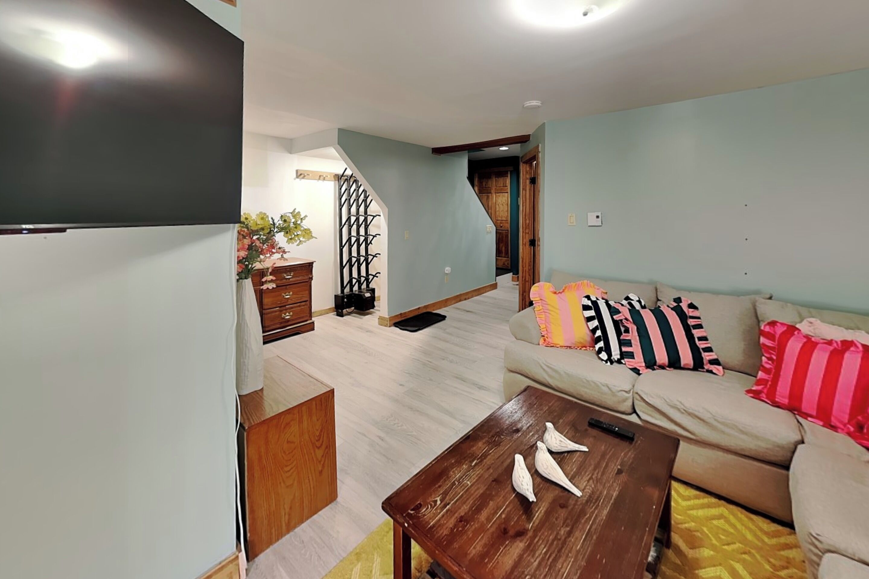 A living room with a sofa, coffee table, and a TV. There is a staircase leading to another room.