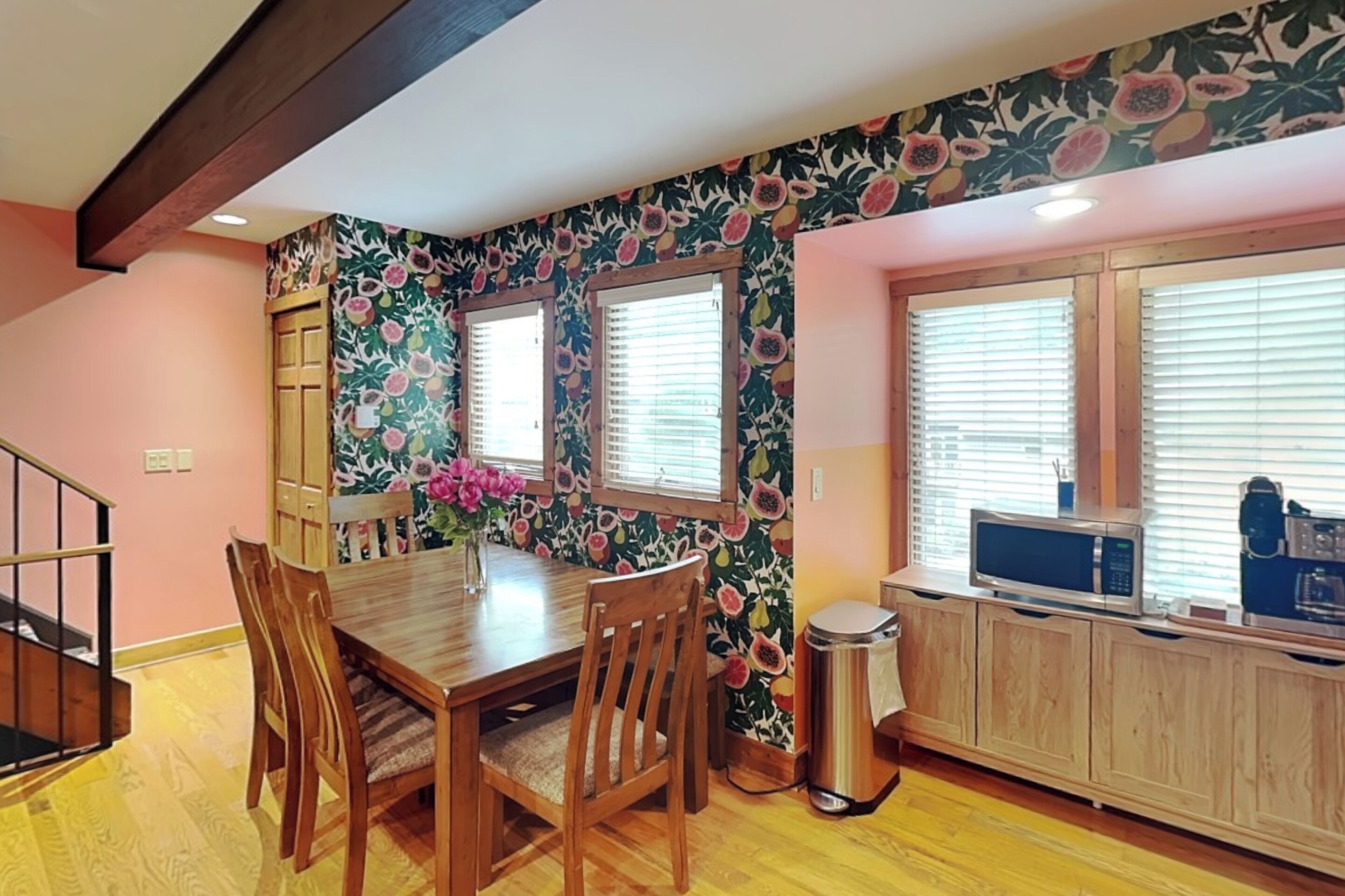 Un comedor con mesa y sillas de madera, un jarrón con flores y una cocina con microondas y armarios.