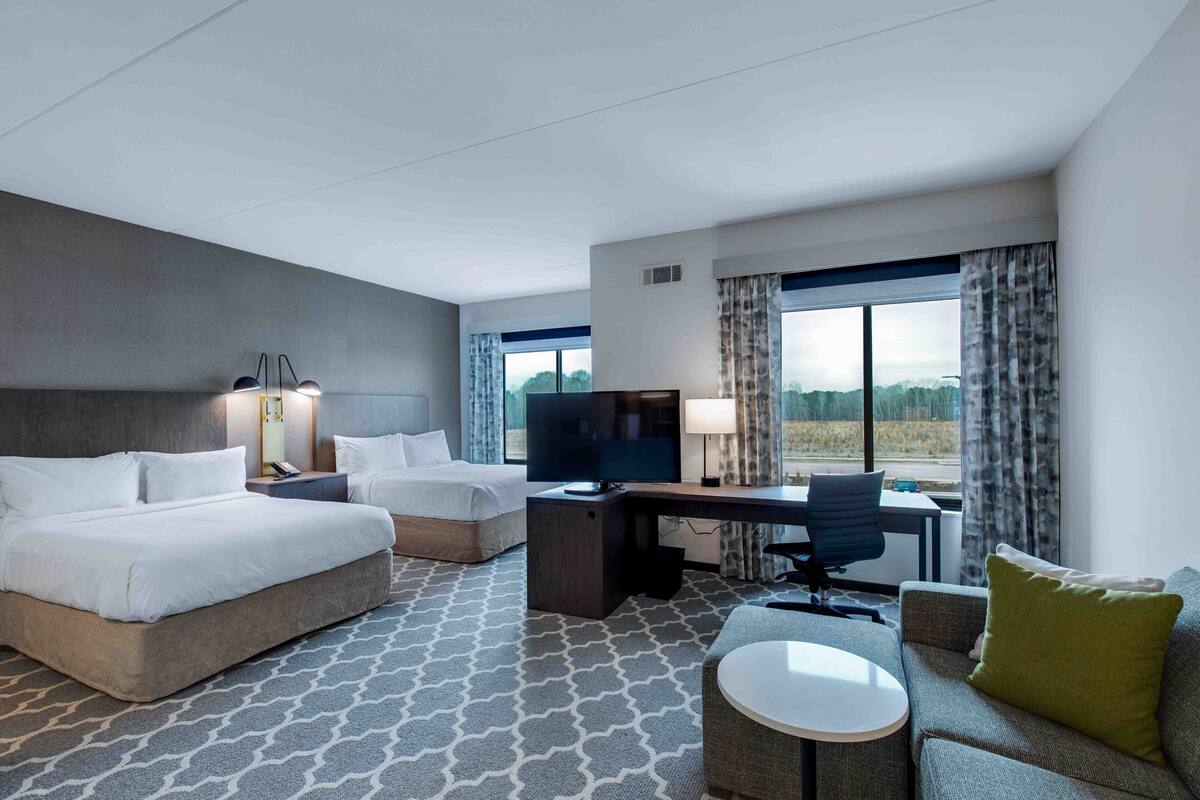 A hotel room with two beds, a desk, a television, and a view of the outdoors.