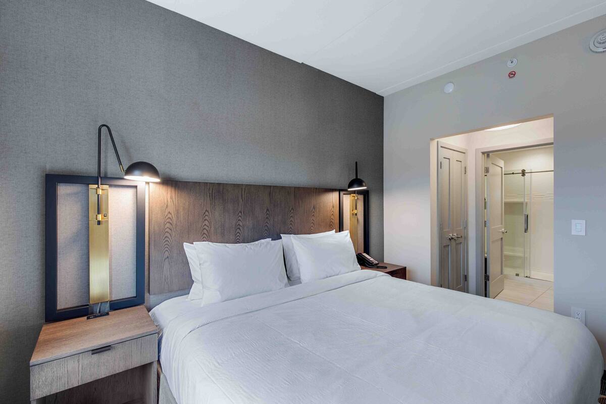 A modern hotel room with a large bed, two bedside lamps, a wooden headboard, and a walk-in closet.