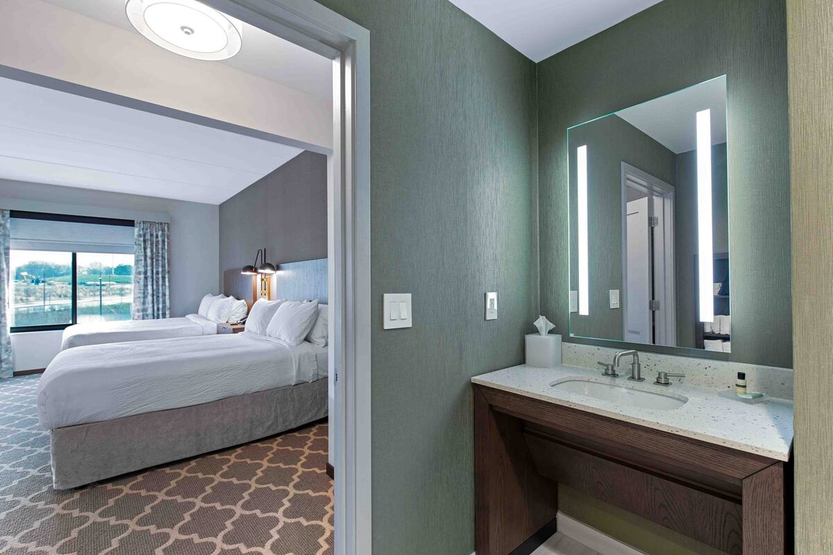 A hotel room with a large bed, a bathroom with a mirror, and a view of the city.