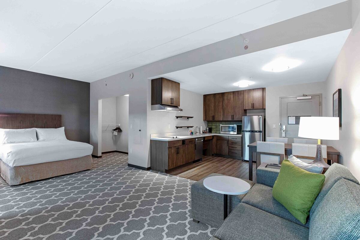 A hotel room with a bed, a small sofa, a coffee table, a kitchenette, and a bathroom.