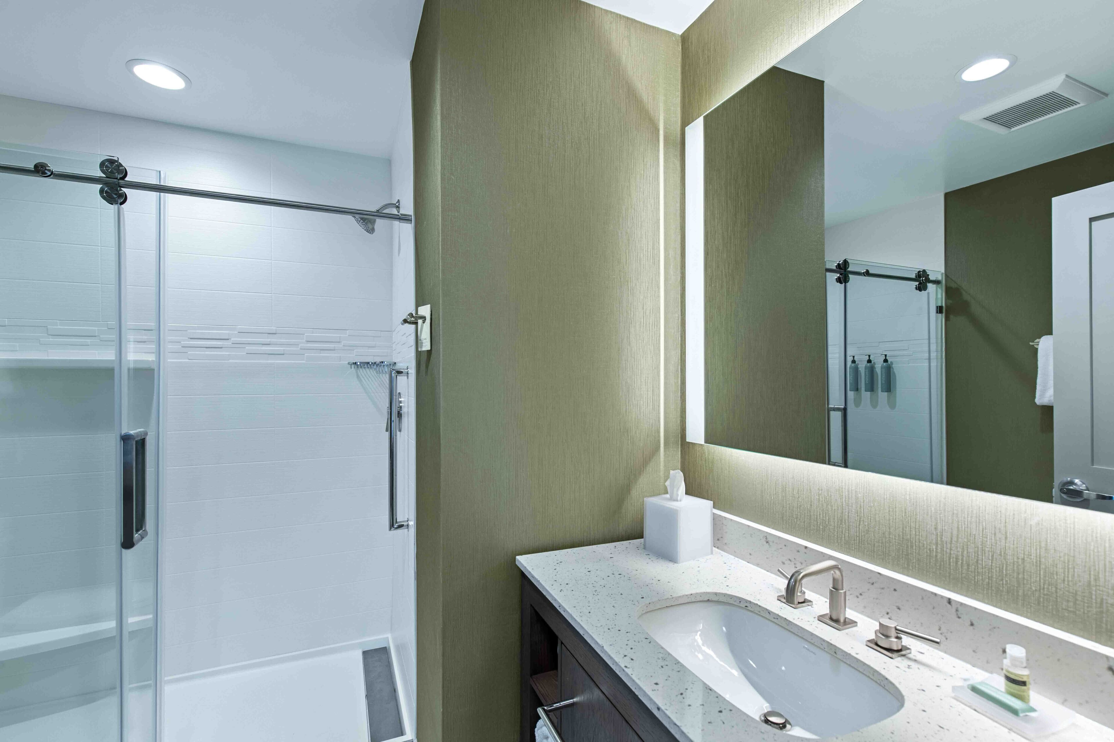 Un baño moderno con cabina de ducha de vidrio, tocador con lavamanos y un espejo grande.