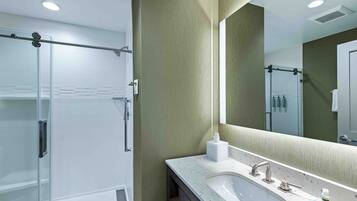 Un baño moderno con cabina de ducha de vidrio, tocador con lavamanos y un espejo grande.