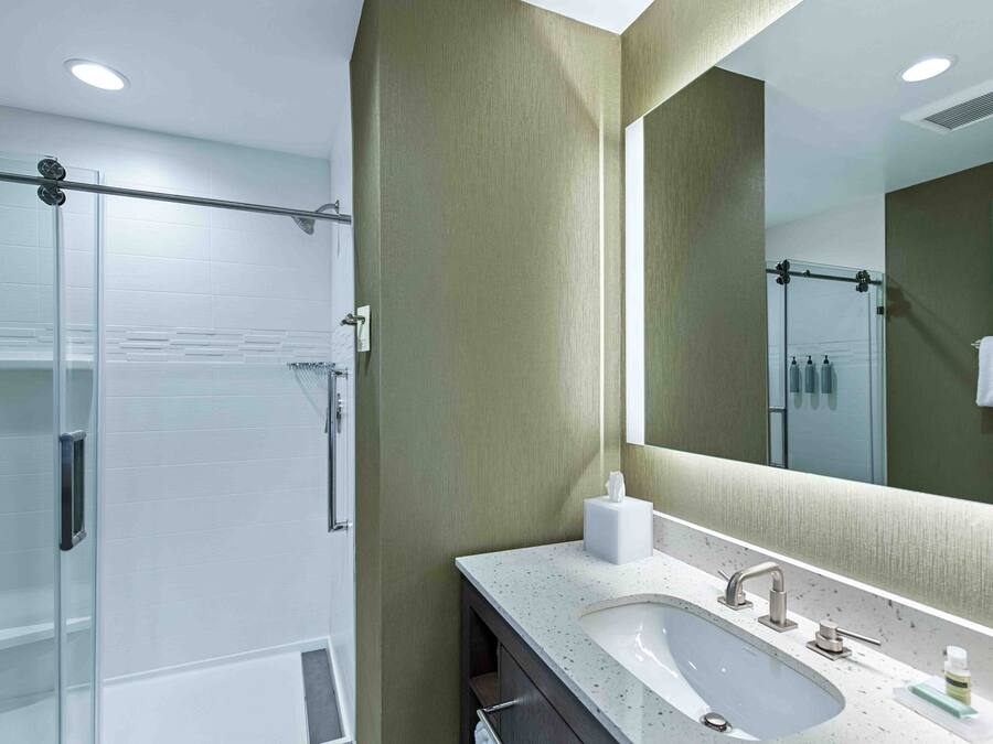Un baño moderno con cabina de ducha de vidrio, tocador con lavamanos y un espejo grande.