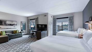 Una habitación de hotel con una cama grande, un sofá, un escritorio con televisor y una ventana con cortinas.