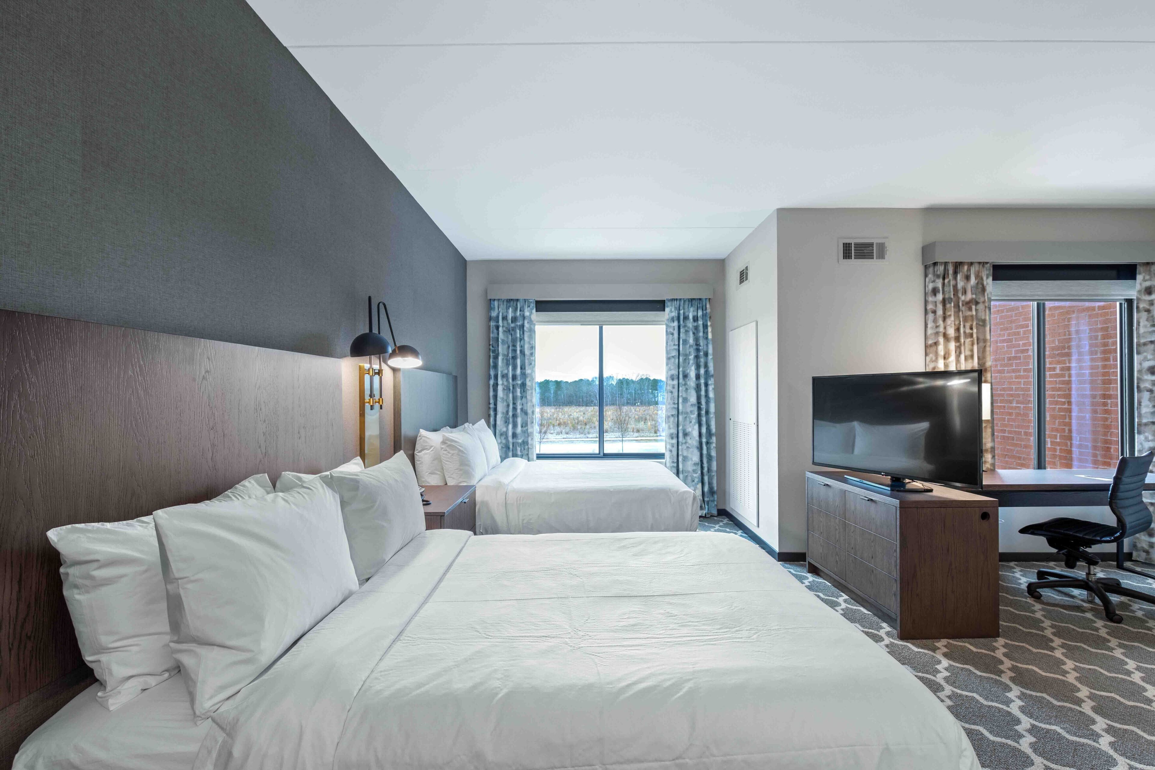 Quarto de hotel com duas camas, uma secretária com televisão e uma janela com cortinas.