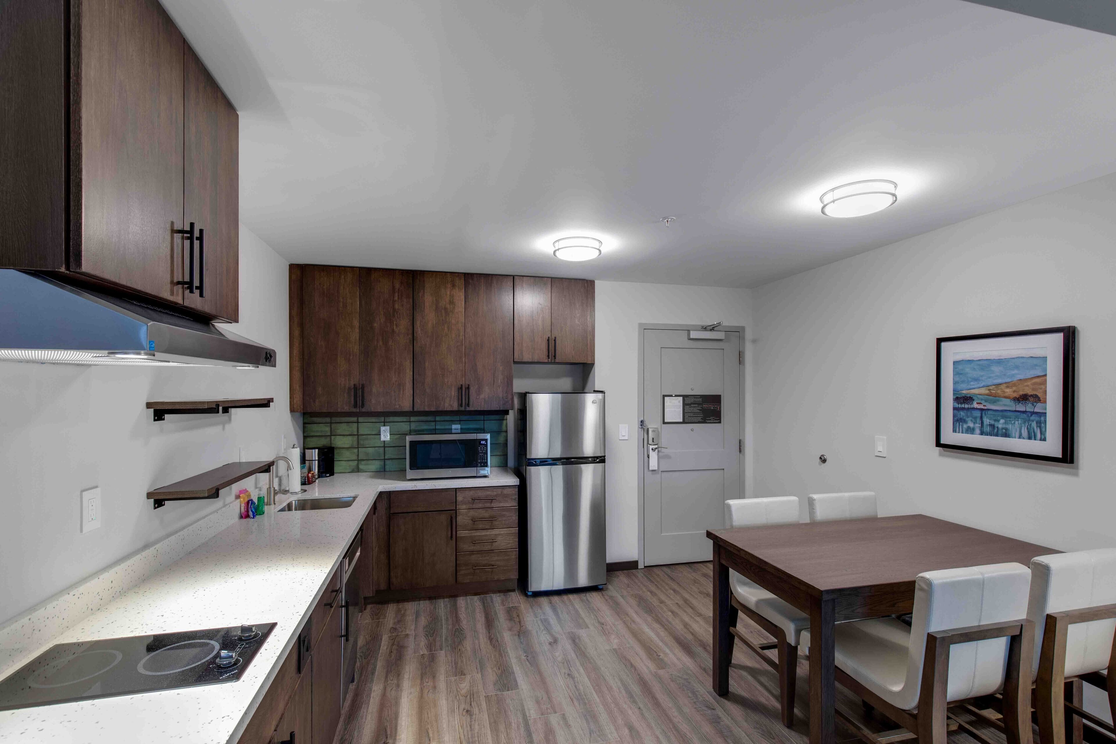 Una cocina moderna con armarios de madera, un refrigerador de acero inoxidable, un microondas y una zona de comedor con una mesa y sillas.