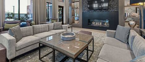 A spacious living room with a large sectional sofa, a glass coffee table, and a stone accent wall with a fireplace.