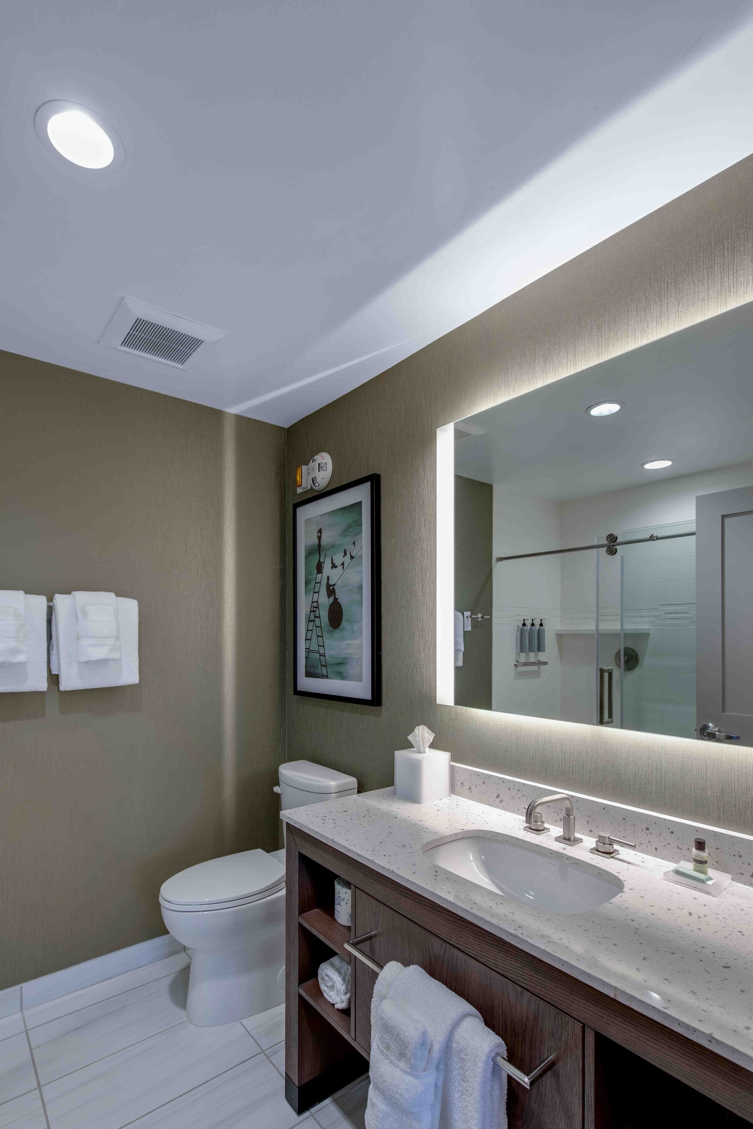 A modern bathroom with a large mirror, a sink, and a toilet.
