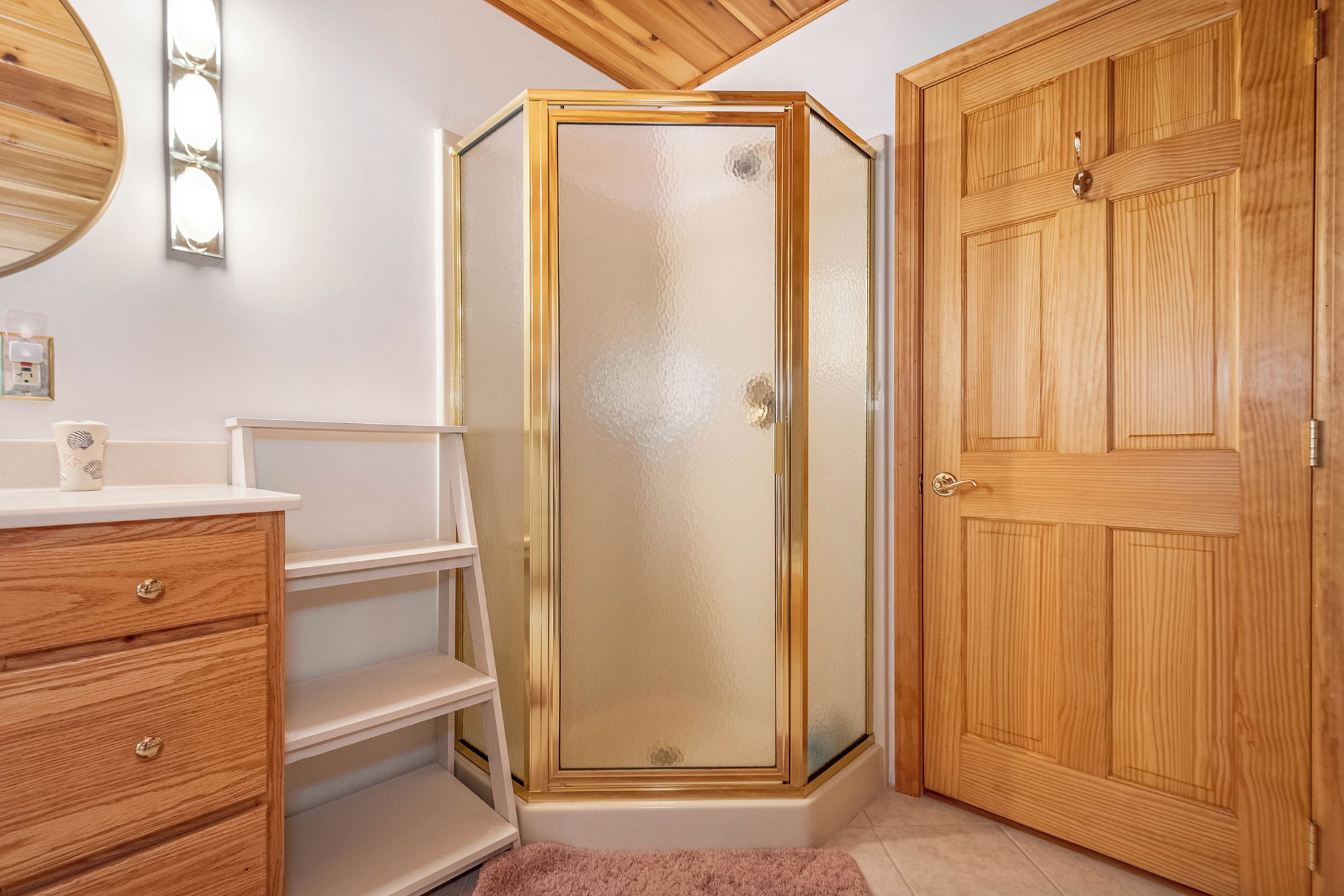 A bathroom with a wooden vanity, a glass shower enclosure, and a wooden door.