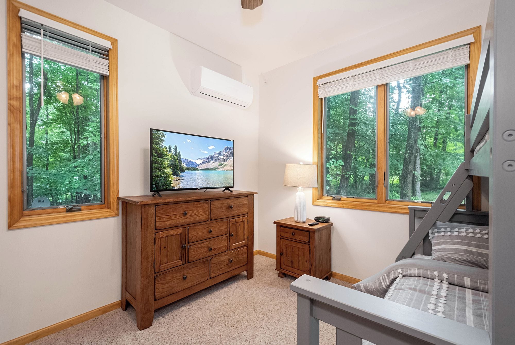 A bedroom with a bed, a wooden dresser, a TV, and a nightstand with a lamp.