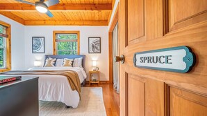 A bedroom with a bed, bedside lamps, a wooden ceiling, and a door labeled "SPRUCE". - Woodhaven by Taylor Made Deep Creek (Swanton)