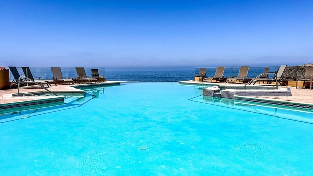 Una piscina a sfioro di colore blu intenso con sedie a sdraio rivolte verso l'oceano, circondata da una terrazza piastrellata.