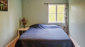 Une chambre à coucher avec un lit, une table de chevet, une fenêtre avec un rideau et un tableau au mur.