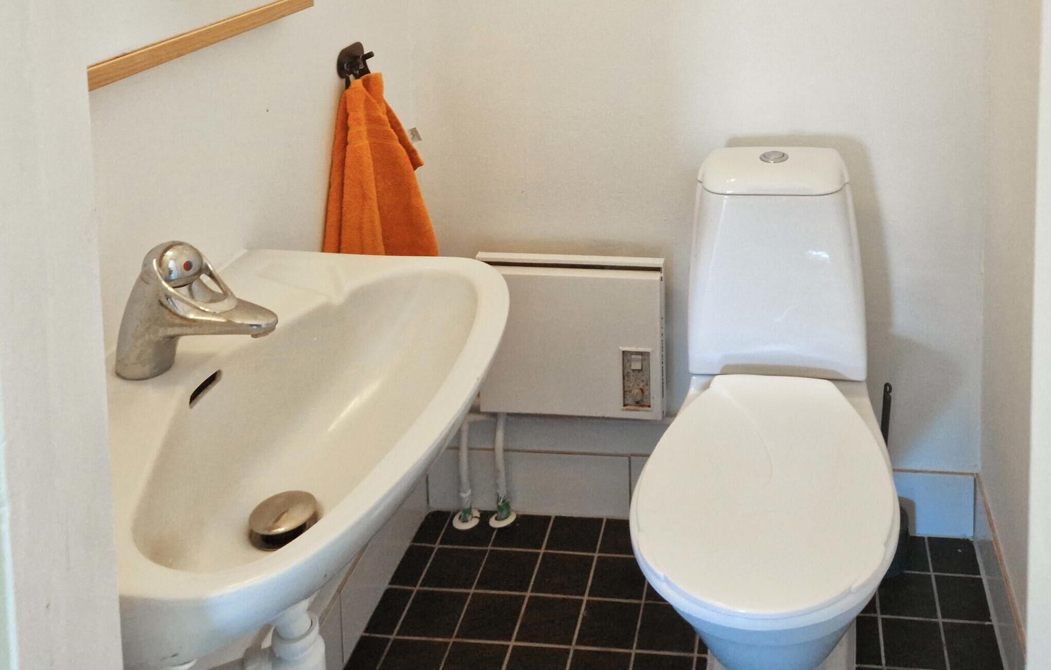 Ein Badezimmer mit einem weißen Waschbecken, einer Toilette und einem Handtuchhalter mit einem orangefarbenen Handtuch.