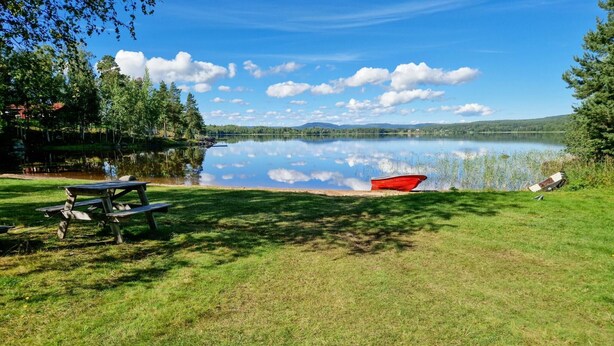 Un espace de pique-nique au bord du lac, avec un bateau rouge, une table de pique-nique et des bancs.