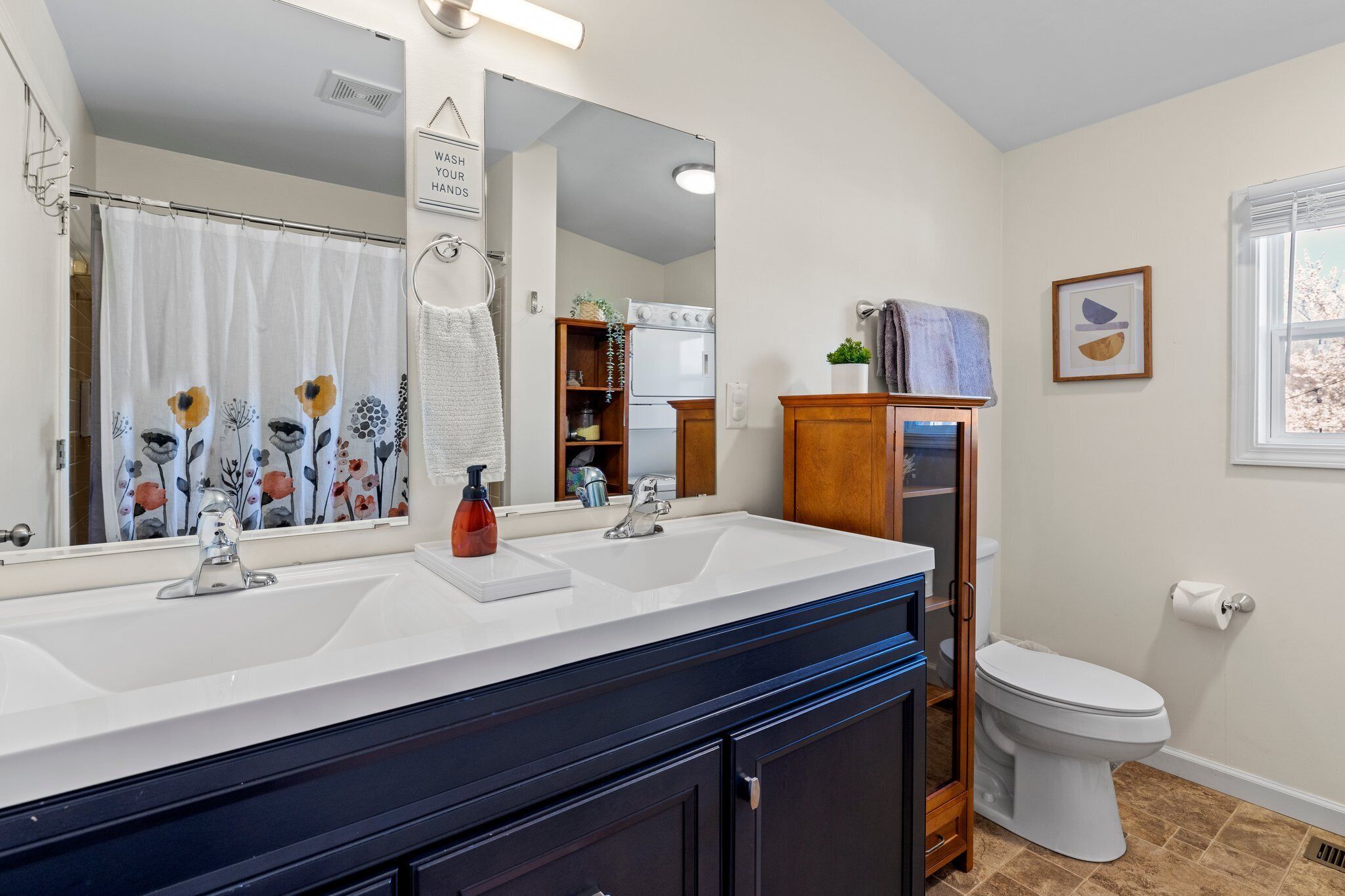 A bathroom with a double sink, a toilet, a mirror, and a shower curtain.