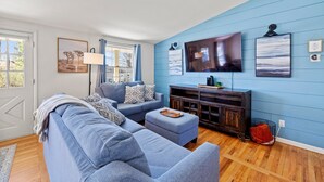 Una sala de estar con una pared azul, un televisor de pantalla plana grande, un sofá, una mesa de centro y piso de madera.