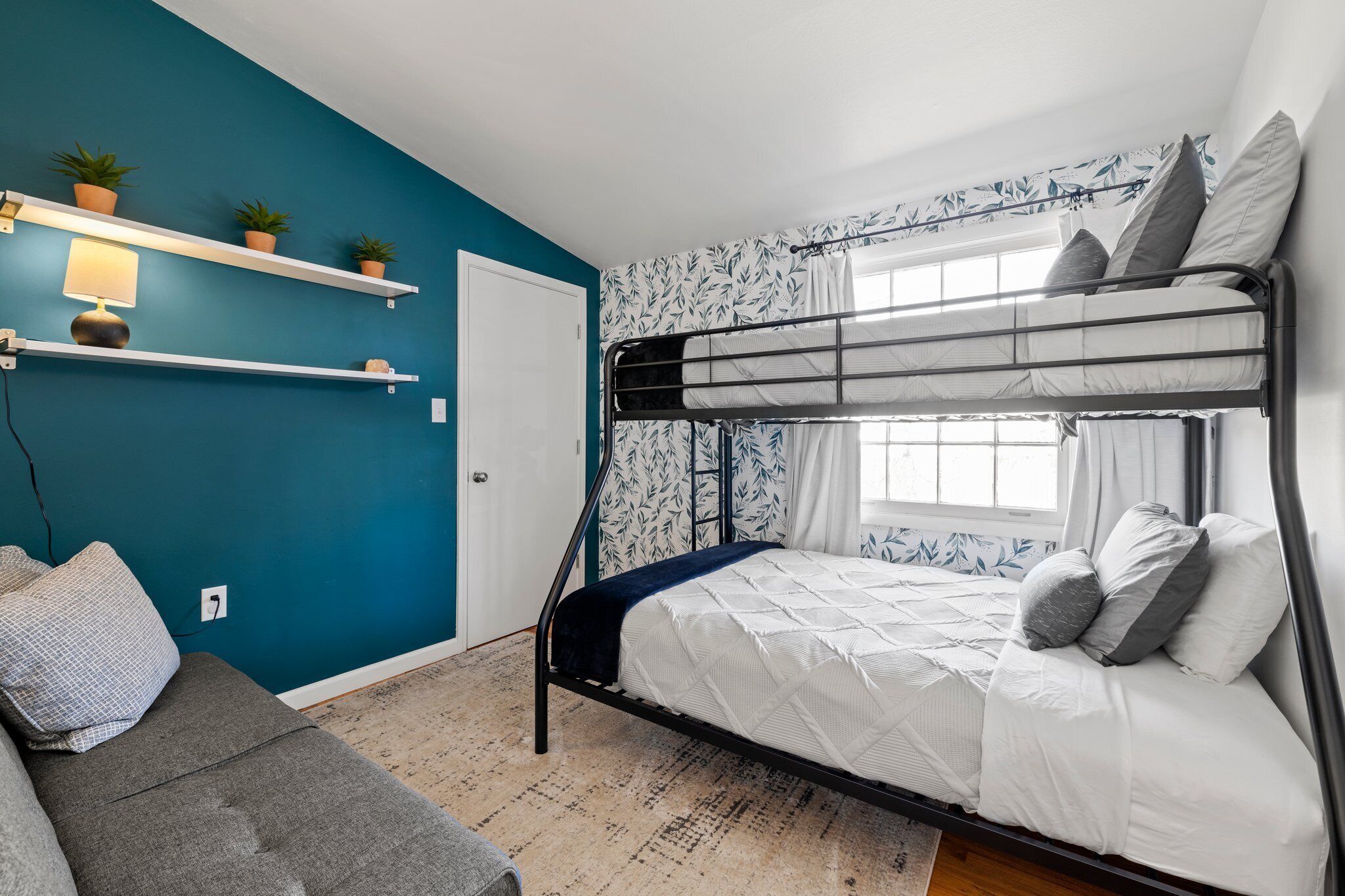 Ein Schlafzimmer mit Etagenbetten, einer türkisblauen Wand, einem Fenster mit Vorhängen und einem grauen Sofa.