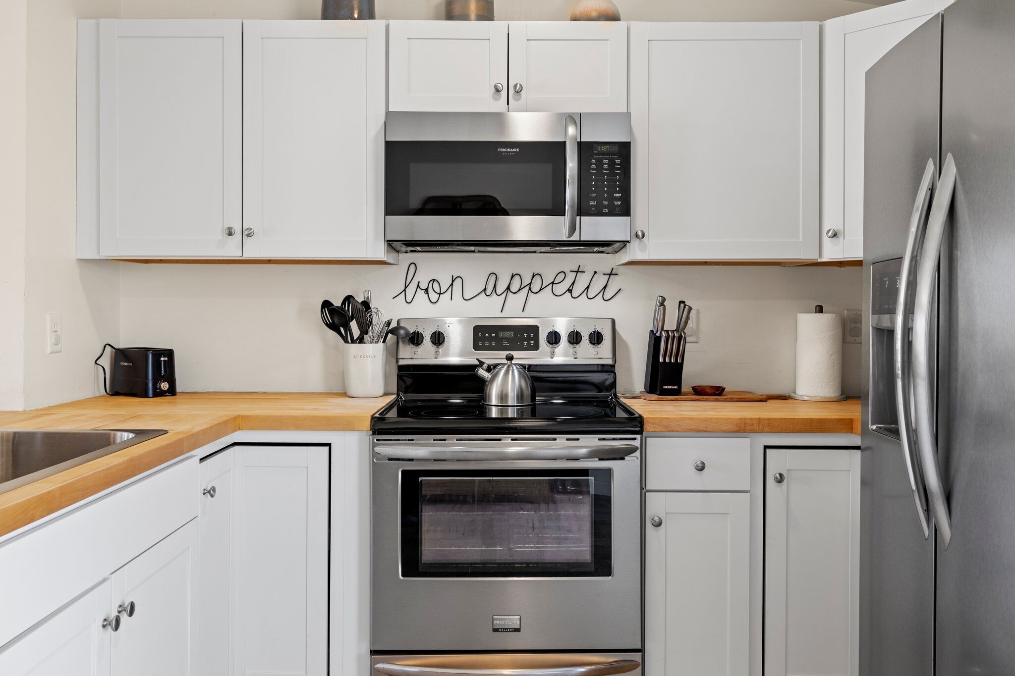 A modern kitchen with white cabinets, a stainless steel microwave, a gas stove, and a built-in oven.