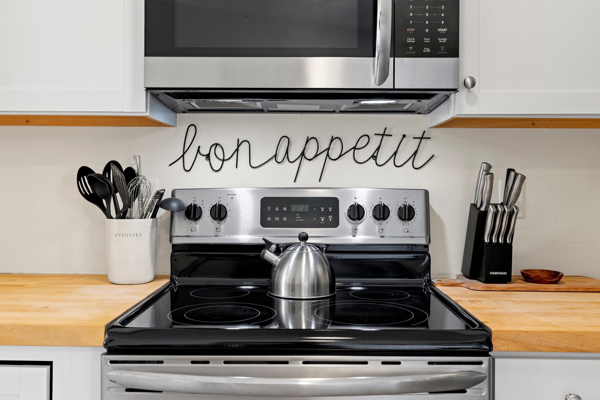 A kitchen with a stove, a kettle, and utensils in a holder.
