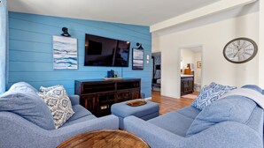 Una sala de estar moderna con una pared azul, un televisor de pantalla plana, un mueble de entretenimiento de madera y un reloj grande.