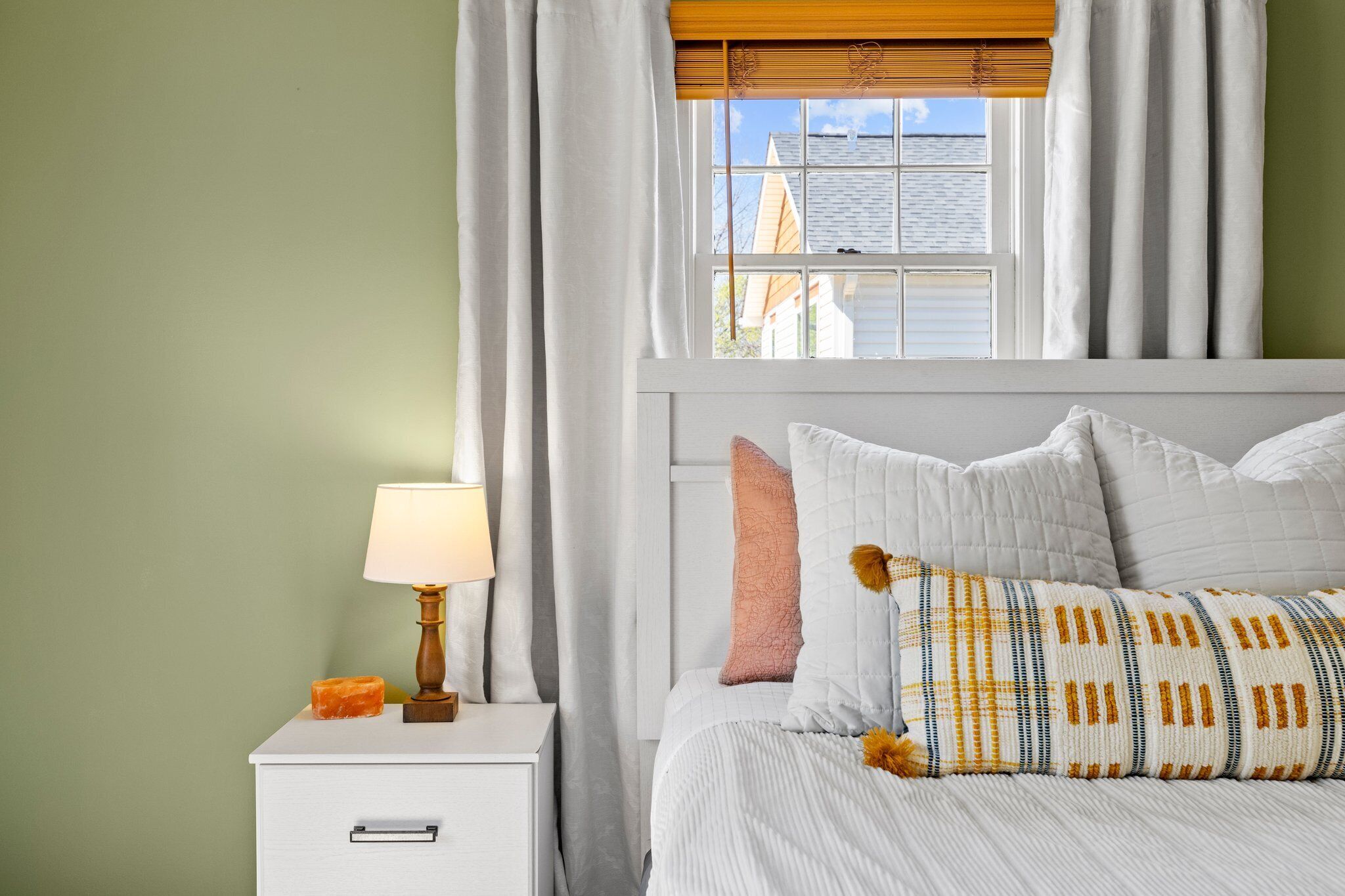 A bedroom with a bed, a nightstand with a lamp, and a window with curtains.