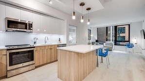 Une cuisine moderne dotée d’appareils électroménagers intégrés, d’un îlot central et d’un coin repas avec des chaises bleues.