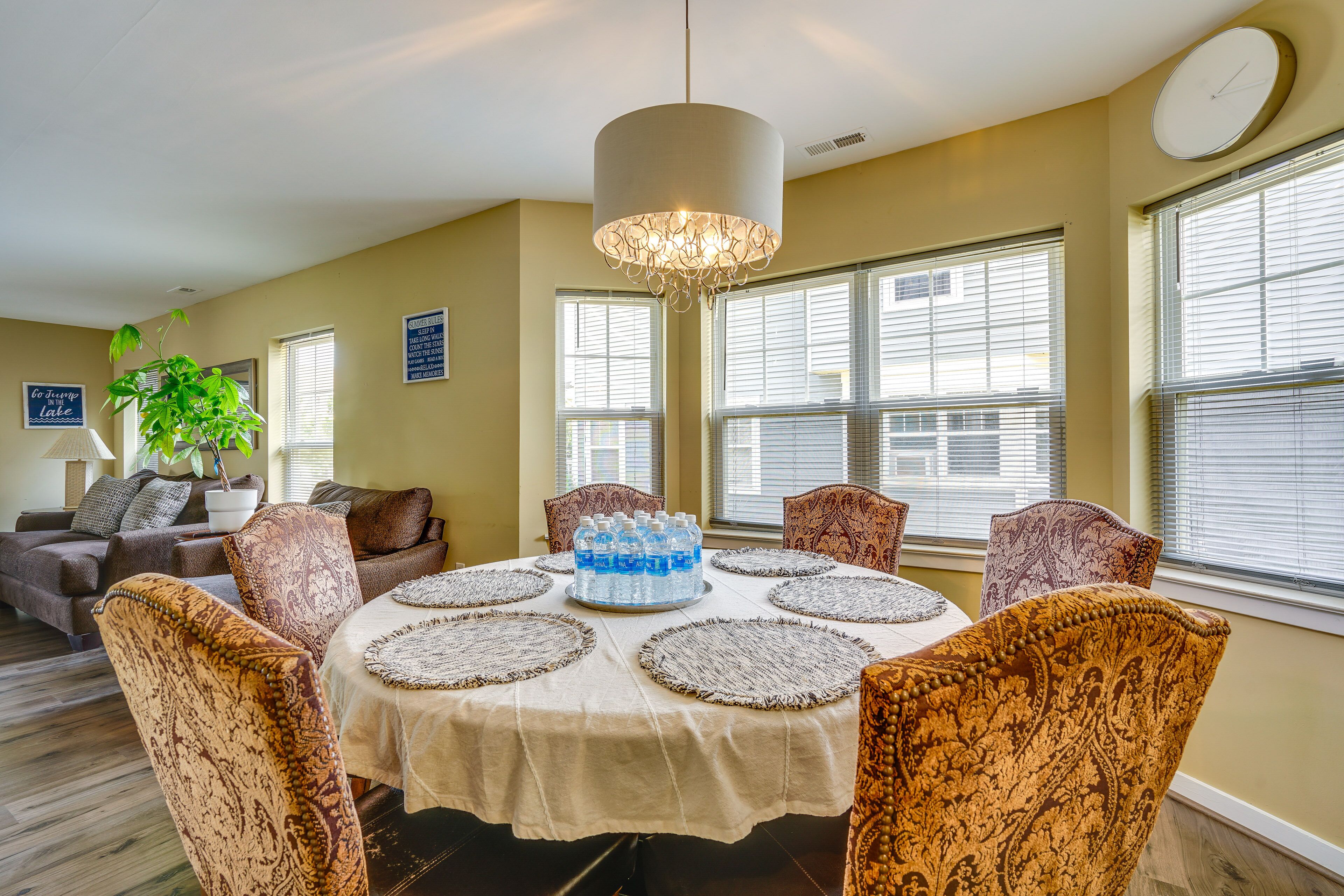 A dining area with a round table, patterned chairs, a chandelier, and a potted plant.