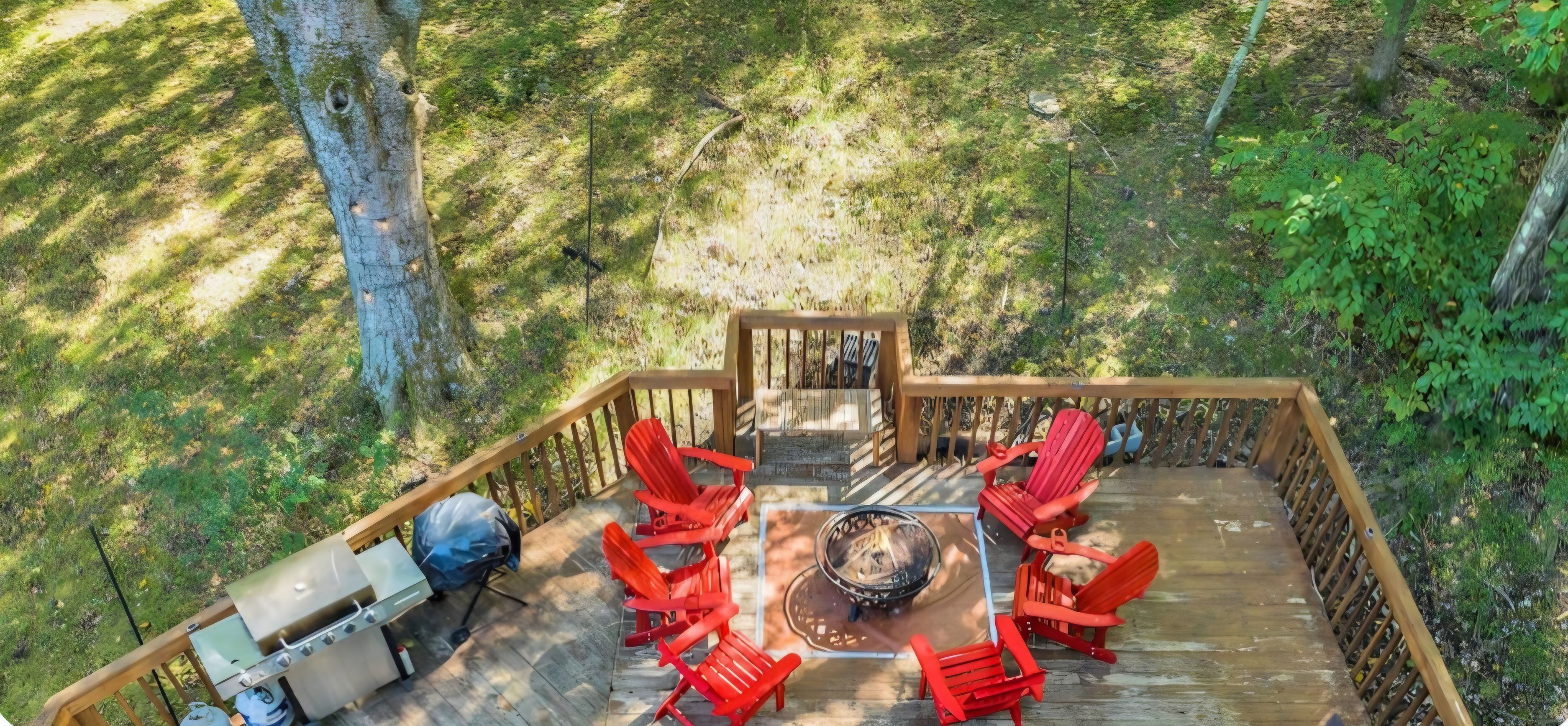 A deck with a grill, red chairs, and a fire pit.