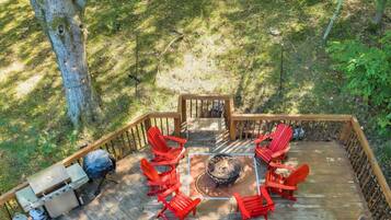 A deck with a grill, red chairs, and a fire pit.