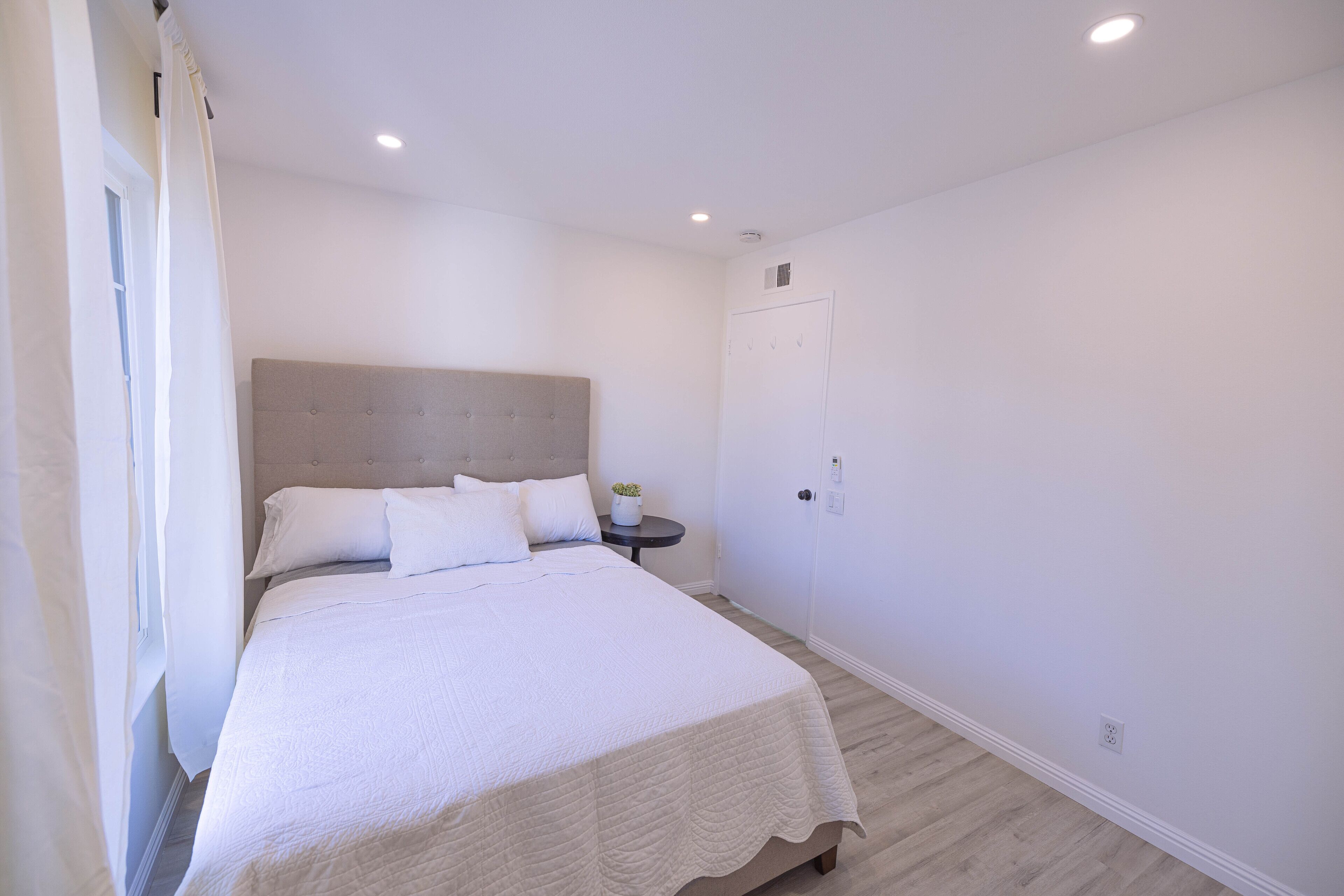 A bedroom with a large bed, a bedside table with a plant, and a door with hooks.