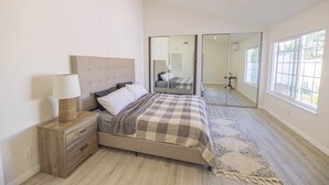 Un dormitorio con cama, mesita de noche, lámpara y un espejo grande.