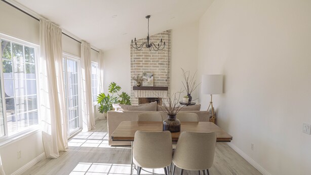 Un comedor con una mesa de madera, cuatro sillas, una araña y una chimenea.