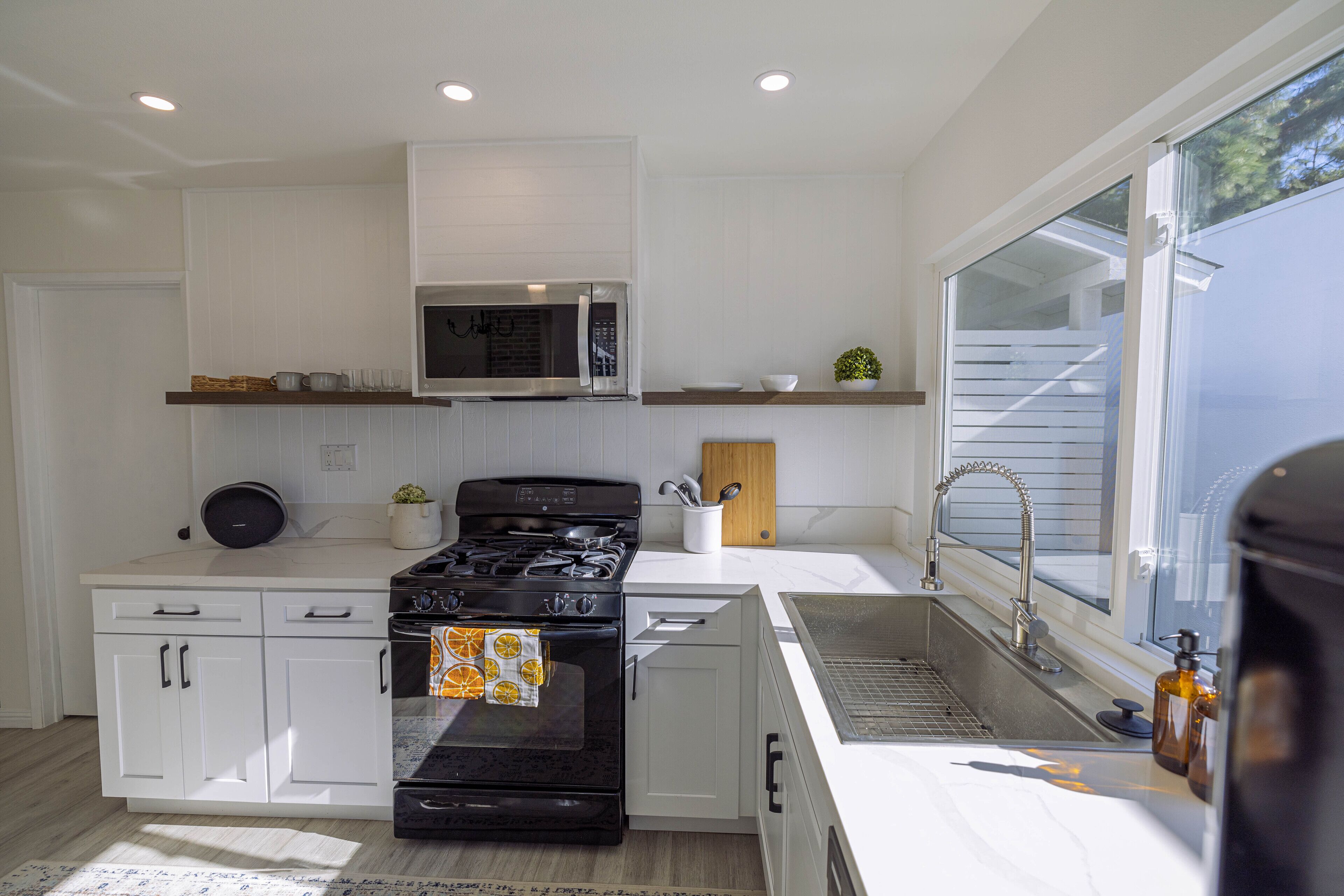 Une cuisine moderne avec des meubles blancs, une cuisinière en acier inoxydable, un four à micro-ondes et une fenêtre équipée de stores.