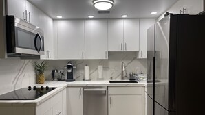A modern kitchen with white cabinetry, a built-in microwave, a coffee maker, and a refrigerator. - Newly remodeled 2 bd/2ba Kaka'ako condo on 25th floor with city/ocean views (Honolulu)