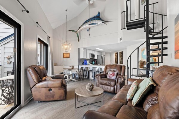 A spacious living area with leather sofas, a coffee table, and a dining area with a kitchen in the background.