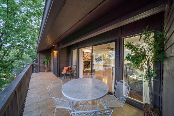 A covered patio with a round metal table and chairs, a stone fireplace, and a glass door leading to an interior space.