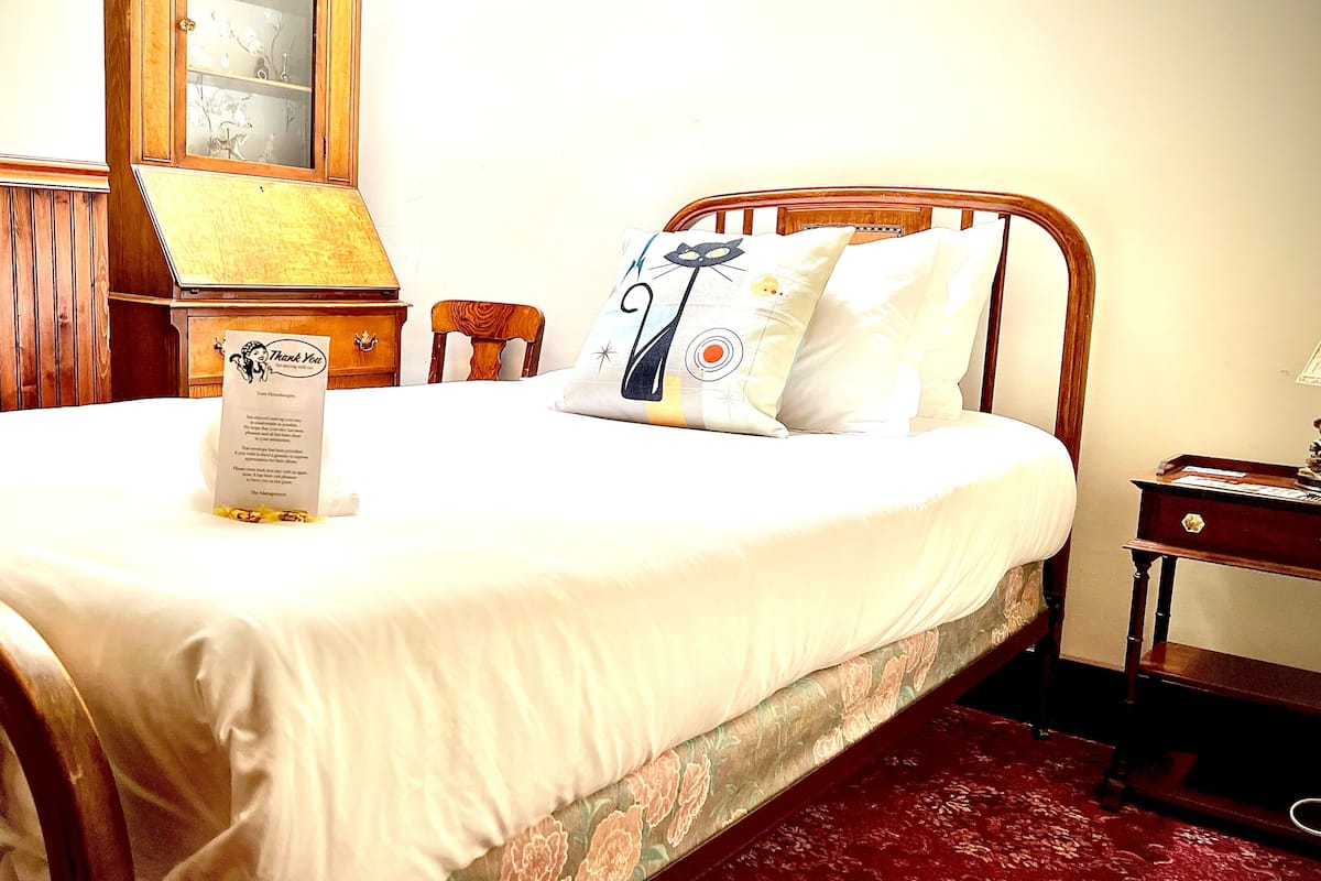 A neatly made bed with a floral-patterned bedspread, a wooden headboard, and a bedside table with a lamp.