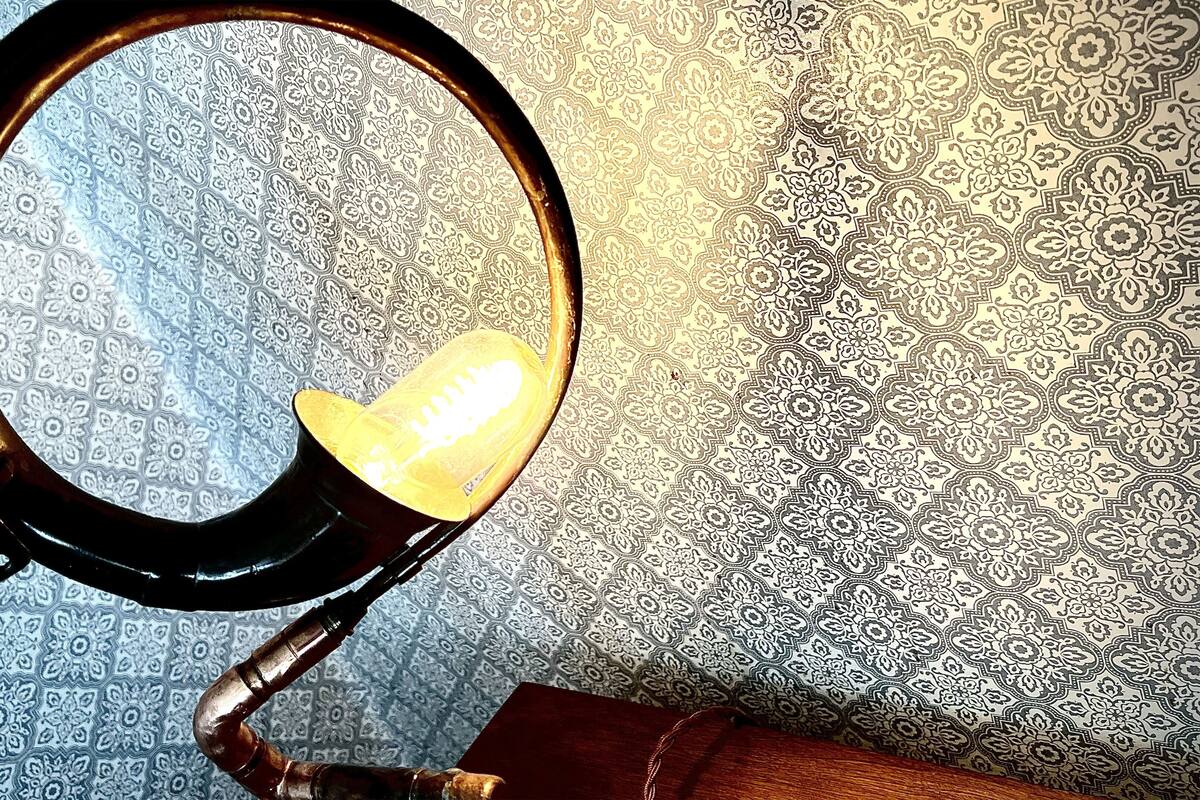 A desk lamp with a round base and a flexible neck, positioned on a patterned wallpaper background.