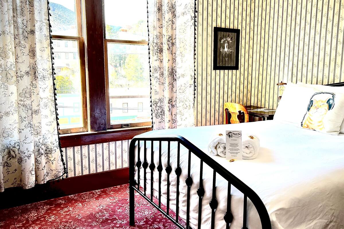 A bedroom with a bed, a window with curtains, a framed picture on the wall, and a red carpet.