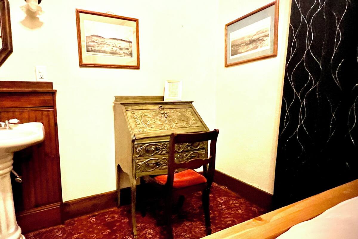 A small room with a white pedestal sink, a wooden cabinet, a chair, and two framed pictures on the wall.